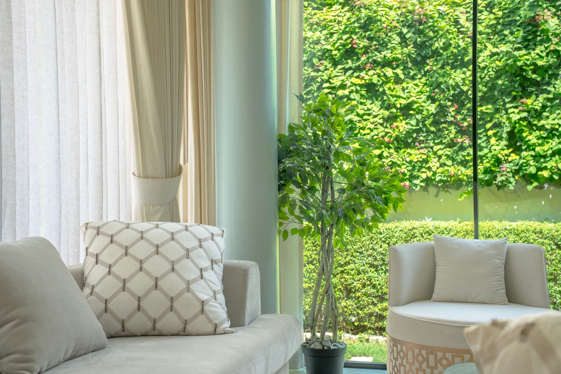 Sitting corner with a lattice cushion and tub chair before full-height glass facing a clipped hedge