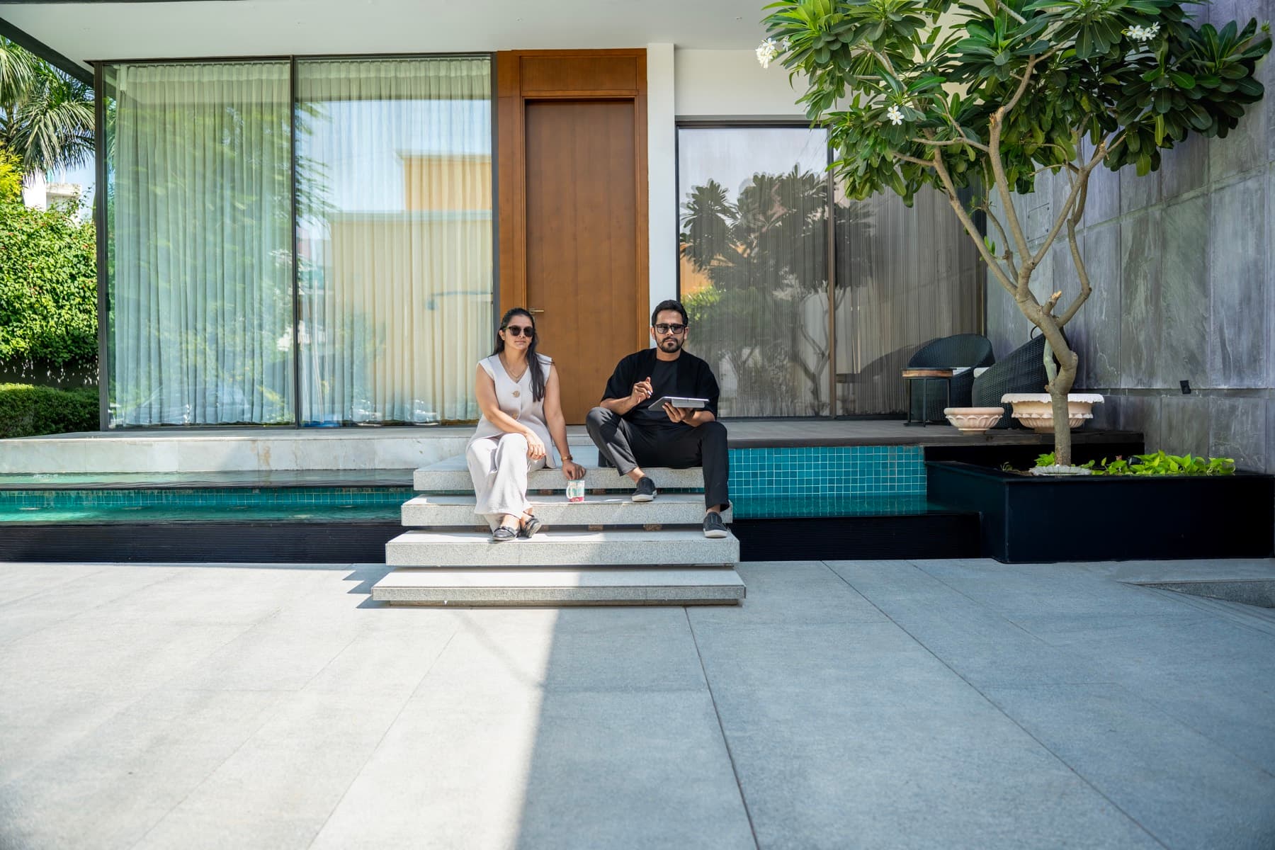 Stone entrance steps crossing the turquoise-tiled water body to the timber door, two people seated