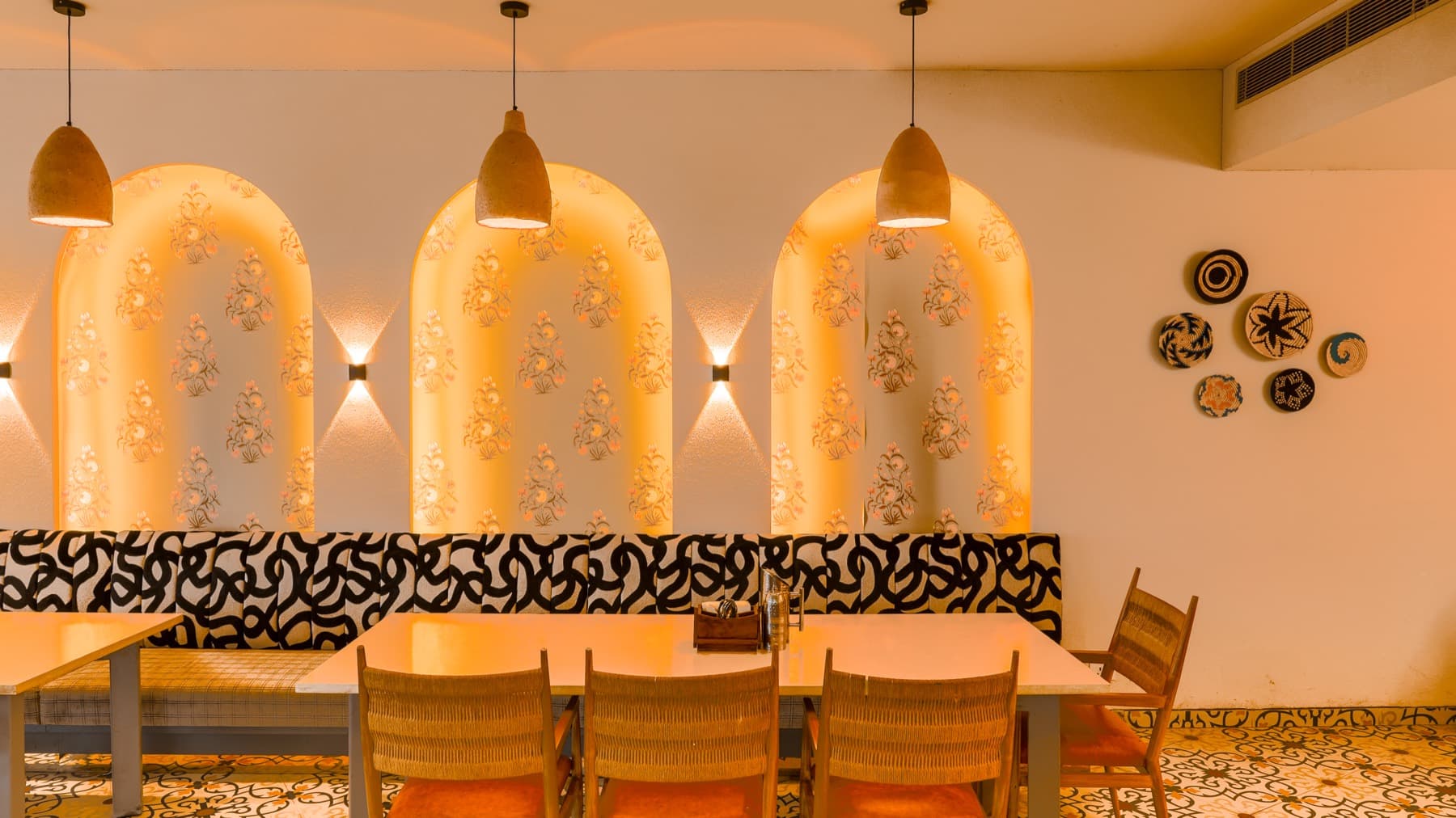 Three backlit arched niches with floral print above a black and cream banquette and rope-woven chairs