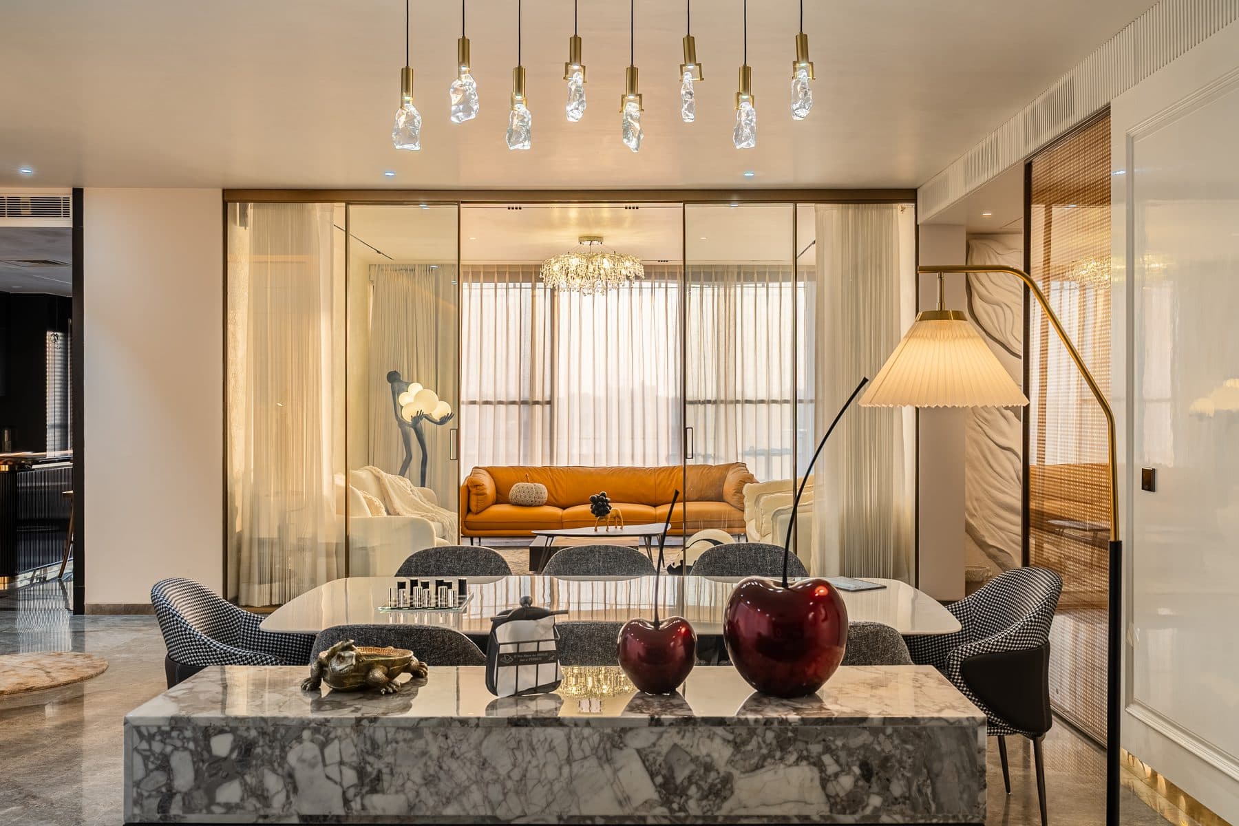 Grey-veined marble island before the dining table and raw-crystal pendants, the drawing room beyond gold-framed glass