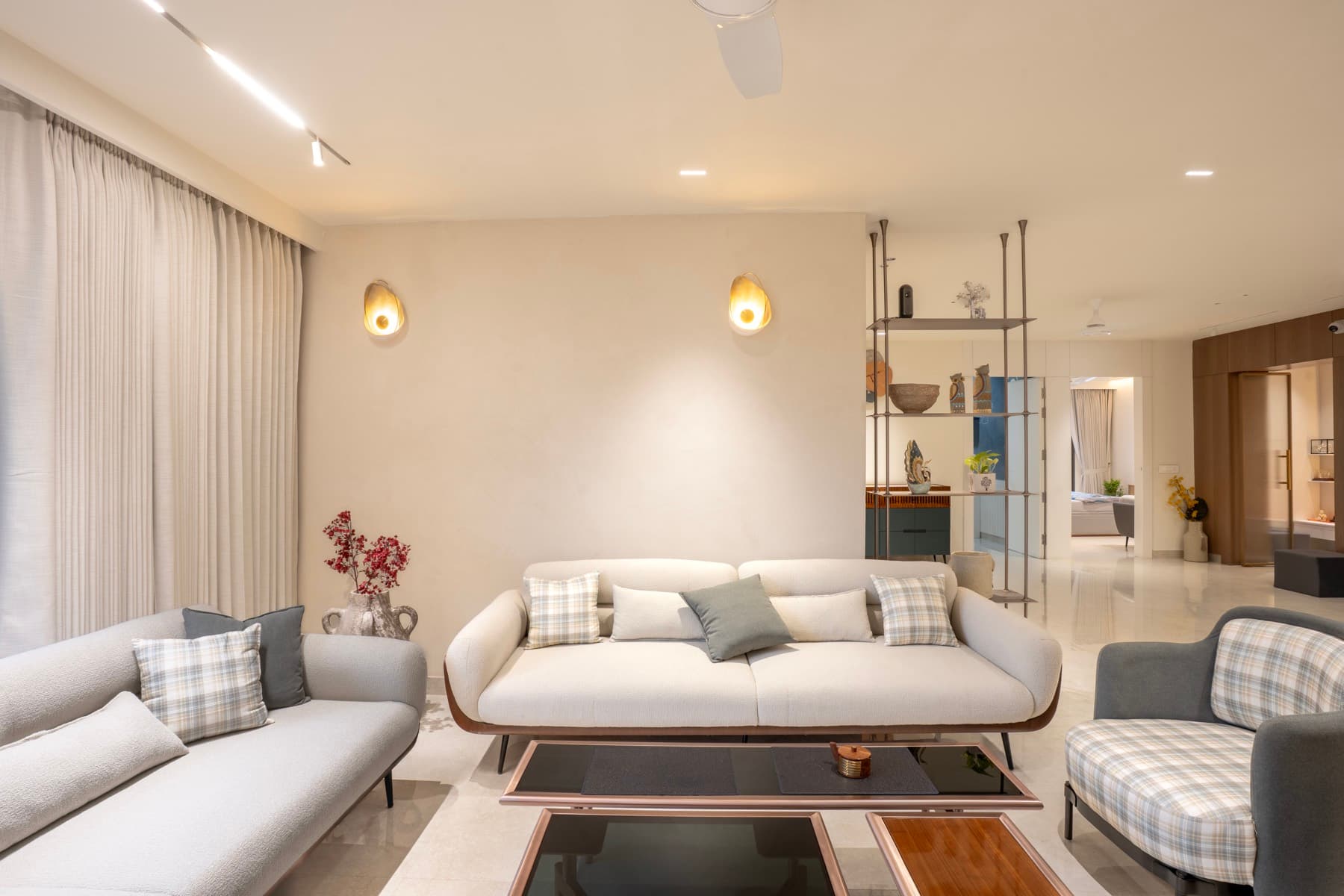 Living room sofas in cream and grey with plaid cushions beneath two brass shell-shaped wall sconces