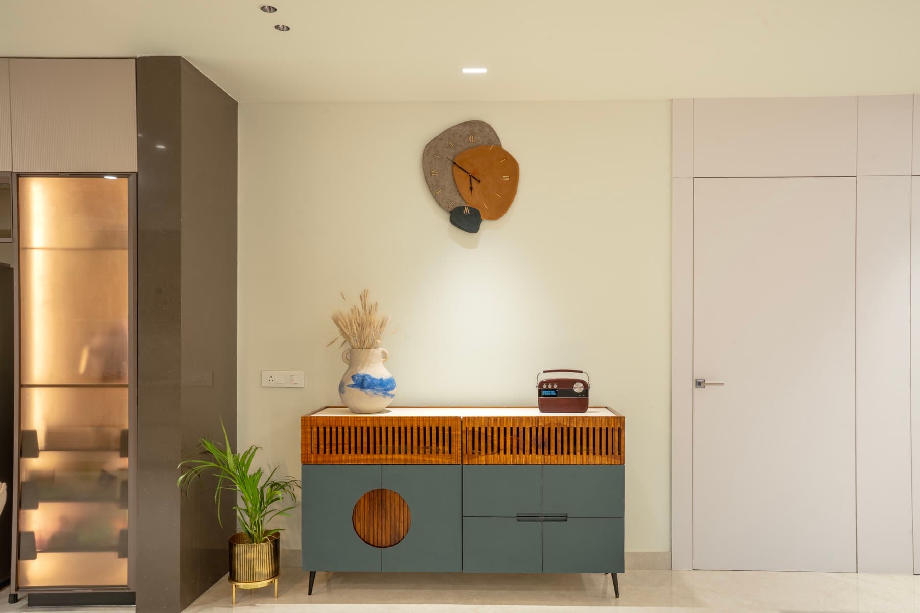 Grey-green sideboard with slatted timber top band and round slatted door, layered wall clock above