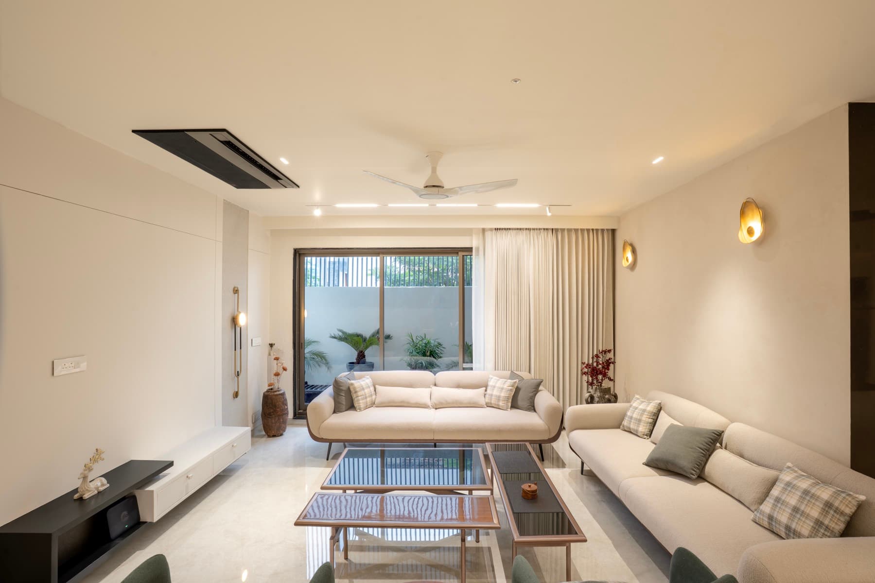 Living room with cream sofas, black glass coffee tables and a sliding door to a planted court