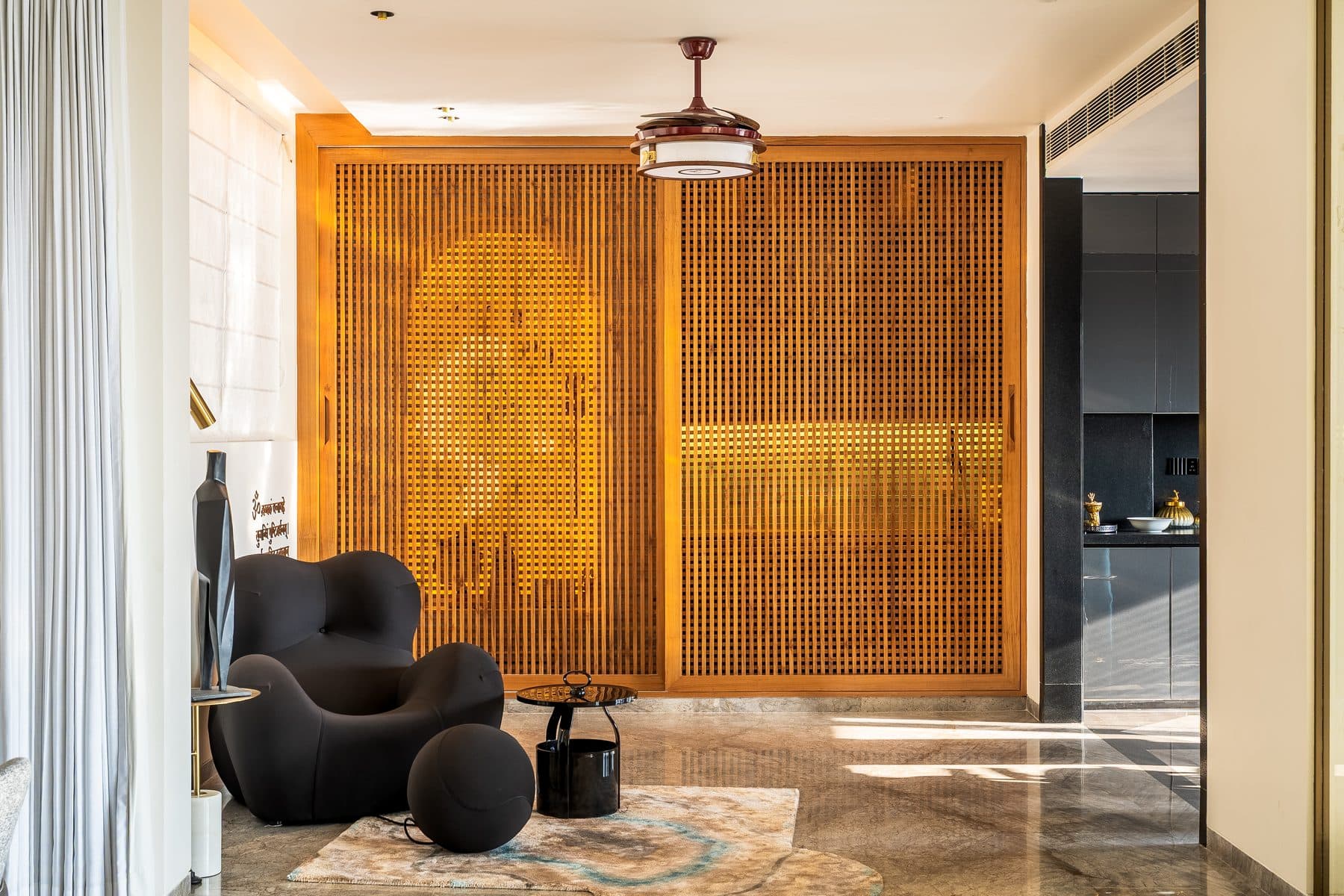 Foyer with a sculptural black armchair and ball ottoman before a closed timber batten sliding screen