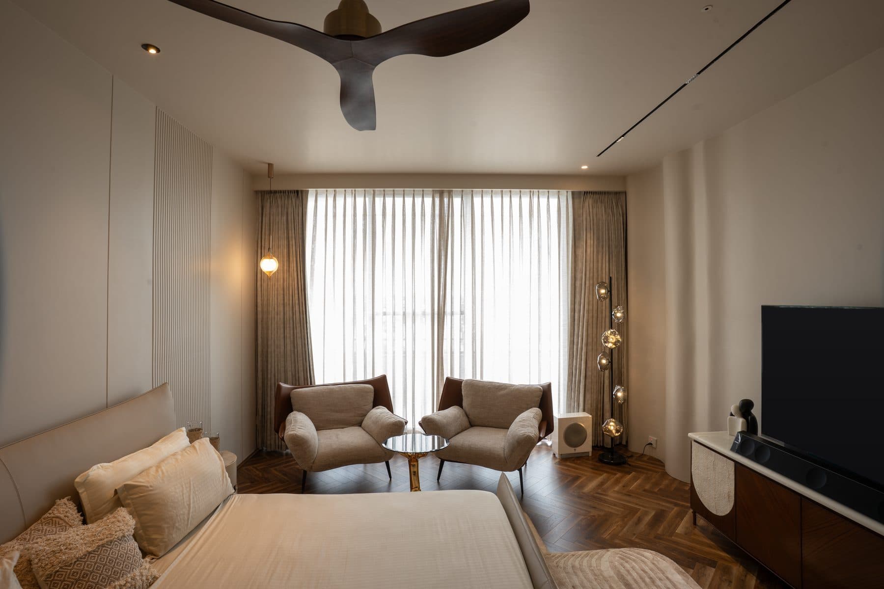 Master bedroom with herringbone parquet, two armchairs by the curtained window and a globe-cluster floor lamp