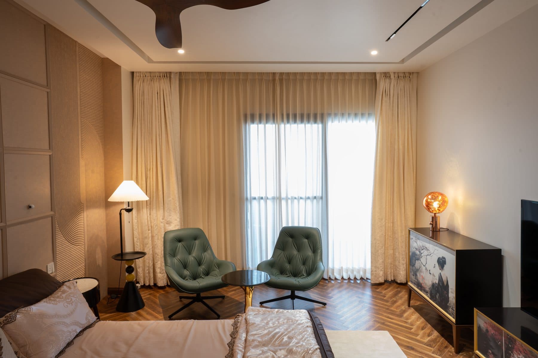 Bedroom with teal tufted armchairs on herringbone parquet and a cabinet painted with a Japanese-style scene