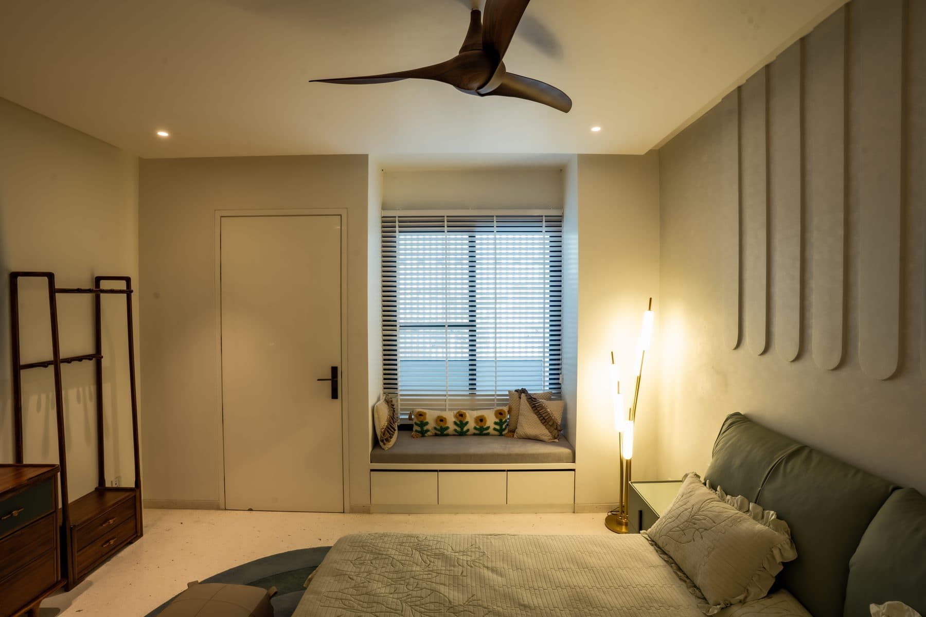 Bedroom with a cushioned window seat, rounded vertical wall panels behind the bed and a gold floor lamp